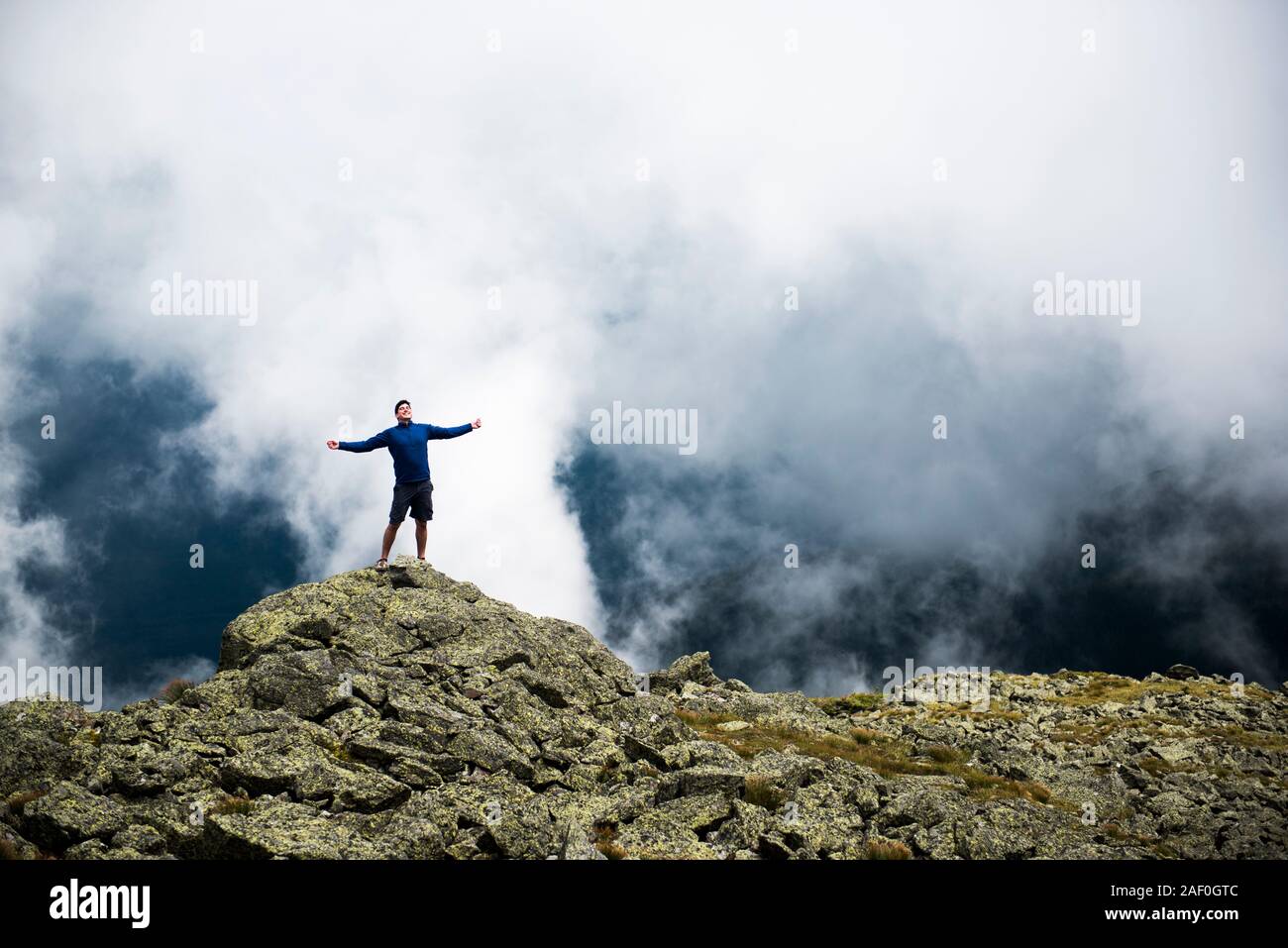 Male hiker enjoying the sun in the mountains with clouds behind Stock Photo