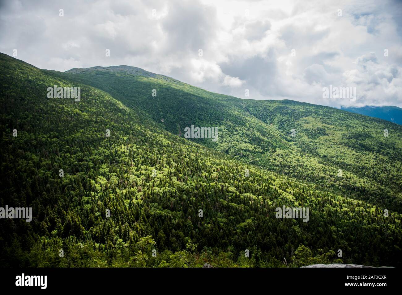 Lush green mountainside with clouds above Stock Photo