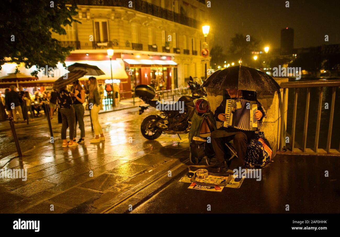 A street performer plays in the night rain on Île Saint-Louis, Paris France. Stock Photo