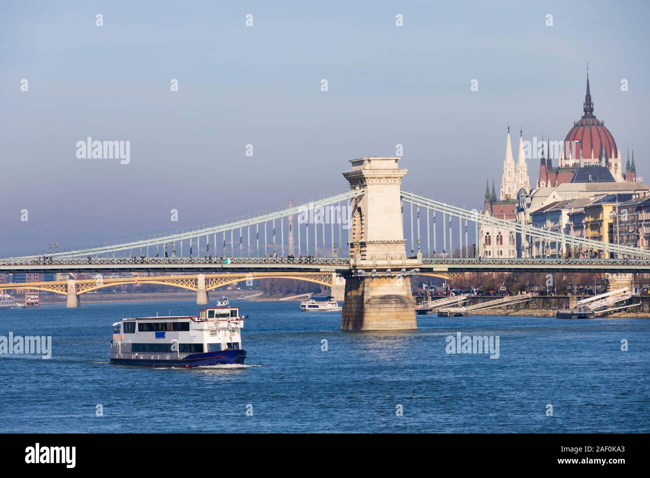 River Danube cruise ship passes under the Chain Bridge with the Parliament building behind. Budapest, Hungary. December 2019 Stock Photo