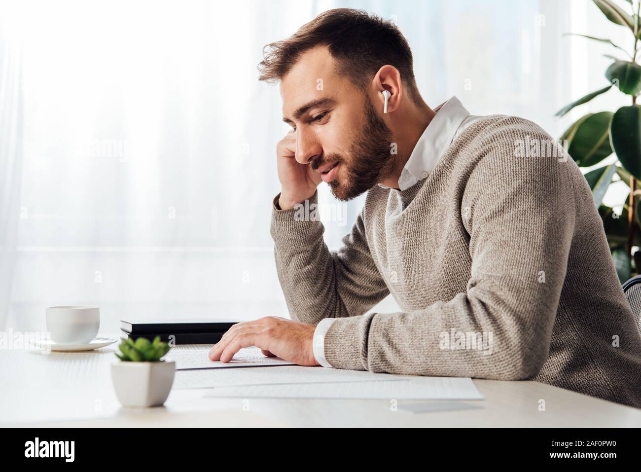 Side view of blind man reading and using wireless earphones at table Stock Photo
