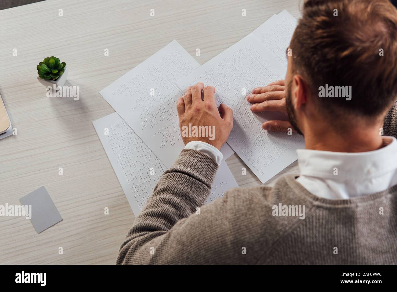 Overhead view of blind man reading braille font beside card with copy space on table Stock Photo