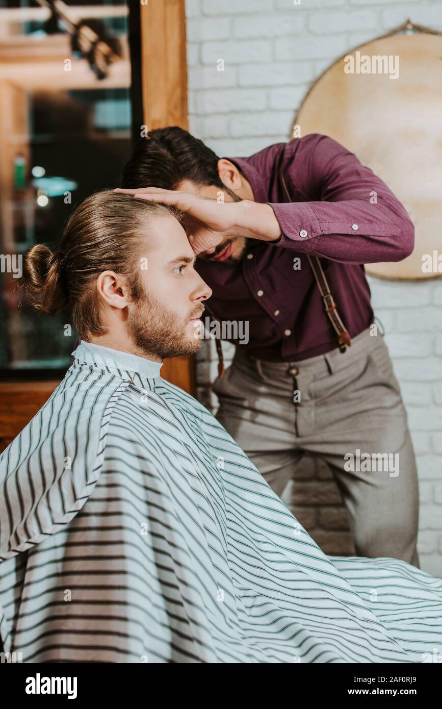 barber styling hair of bearded man in barbershop Stock Photo