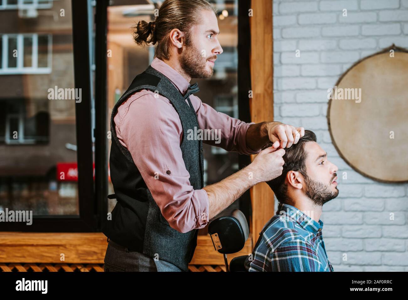 side view of barber styling hair on cheerful bearded man Stock Photo