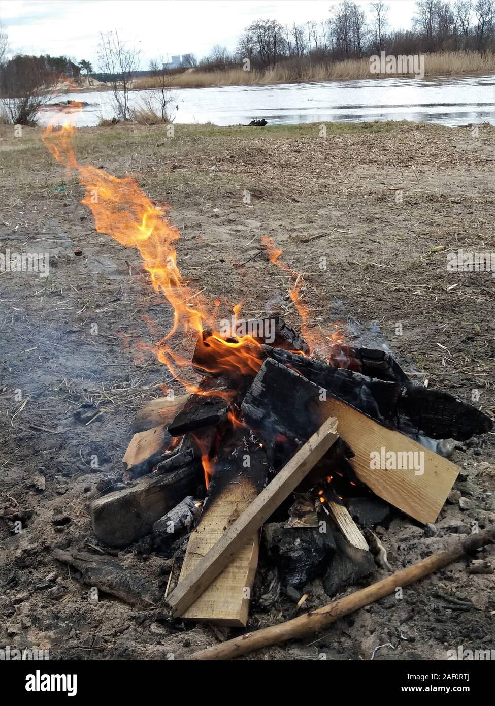 On the shore of a small lake or river, someone collected garbage on the shore and made a fire. Burning garbage. Ecological catastrophy. The problem of ecology. Stock Photo