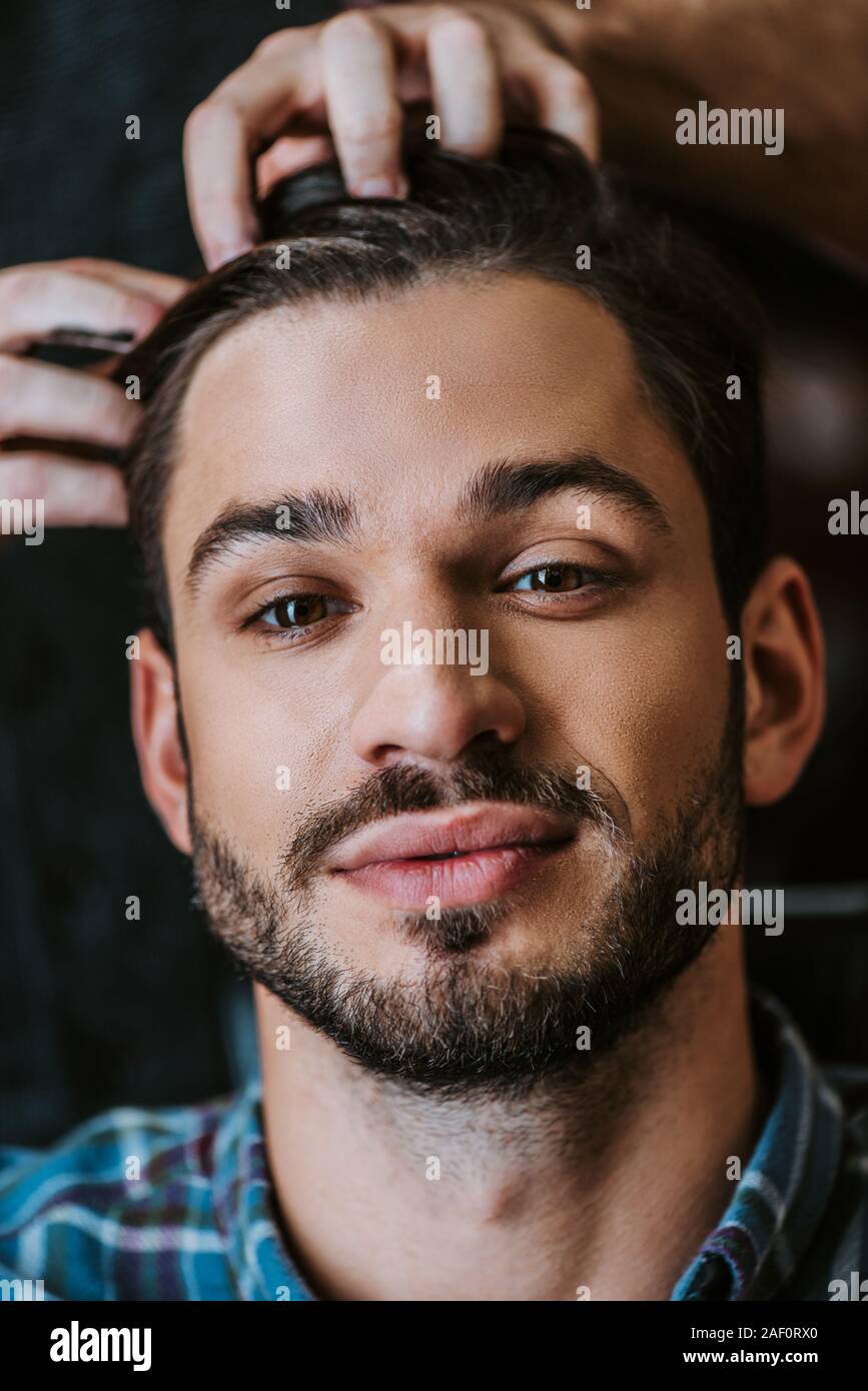 barber with black hair pomade on hands styling hair of bearded man Stock Photo