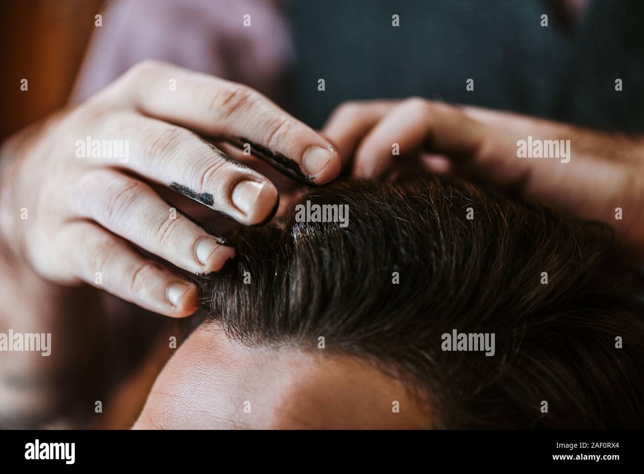 cropped view of barber with black hair pomade on hands styling hair of man Stock Photo