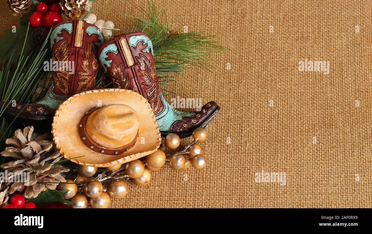 blue and brown cowboy boots and hat with pine, pine cones and berries on a tan textured background with copy space Stock Photo