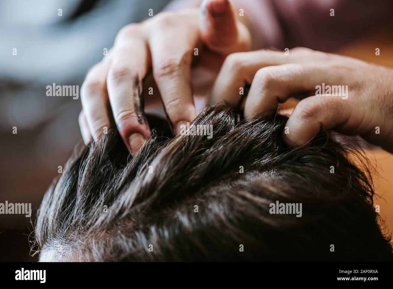 cropped view of barber with black hair pomade on hands styling hair of man in barbershop Stock Photo