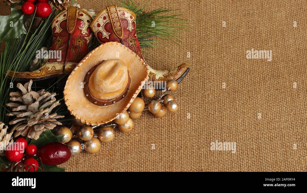 tan and brown cowboy boots and hat with pine, pine cone and berries on a tan textured background with copy space Stock Photo