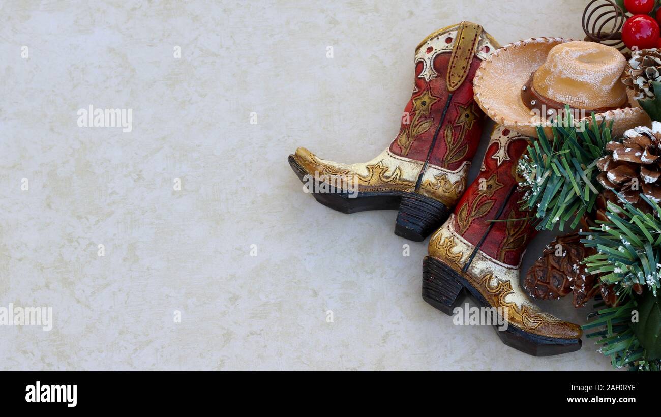 brown and tan rustic cowboy boots and hat with christmas decorations laying on a tan background with copy space Stock Photo