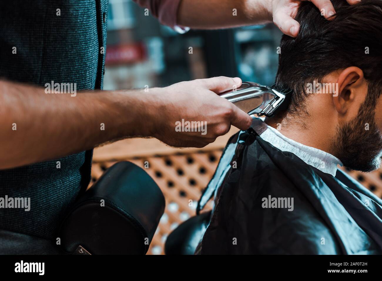 selective focus of barber holding trimmer while styling hair of man Stock Photo
