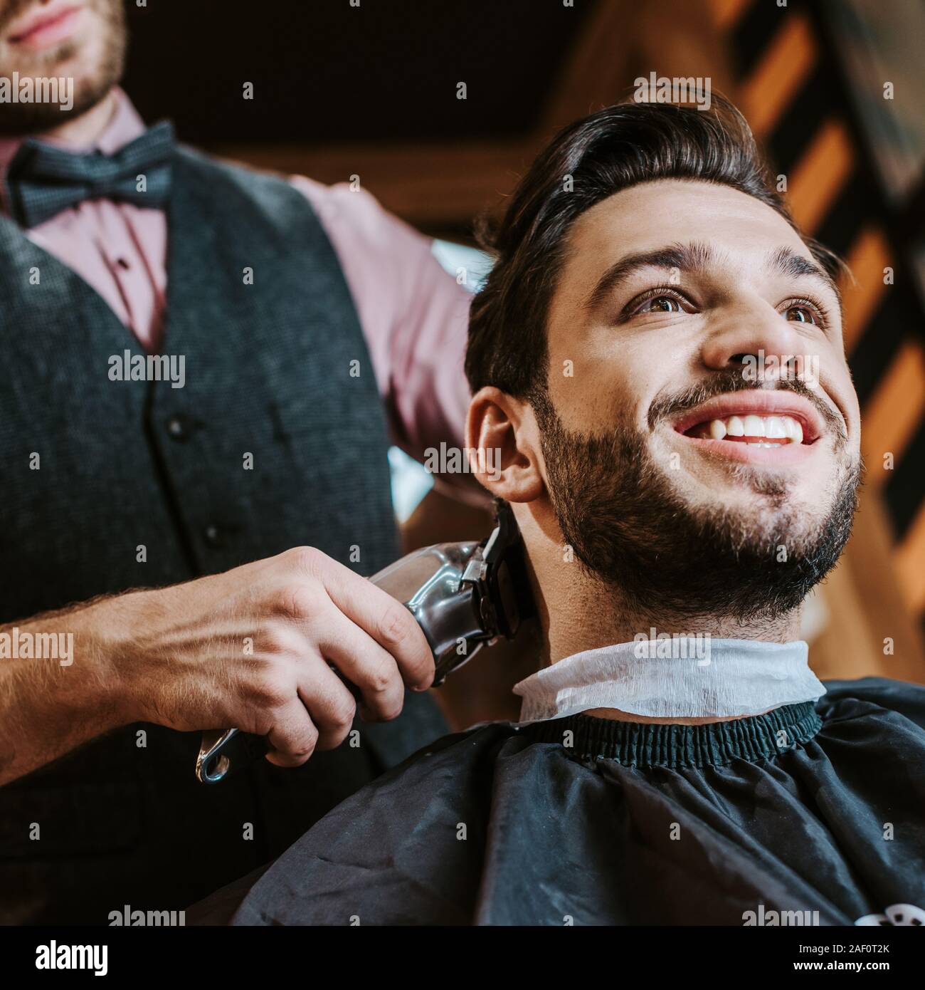 low angle view of barber holding trimmer while styling hair of happy man in barbershop Stock Photo