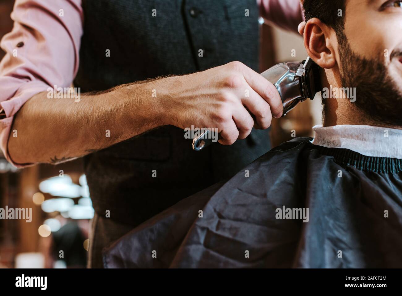 cropped view of barber holding trimmer while styling hair of bearded man in barbershop Stock Photo
