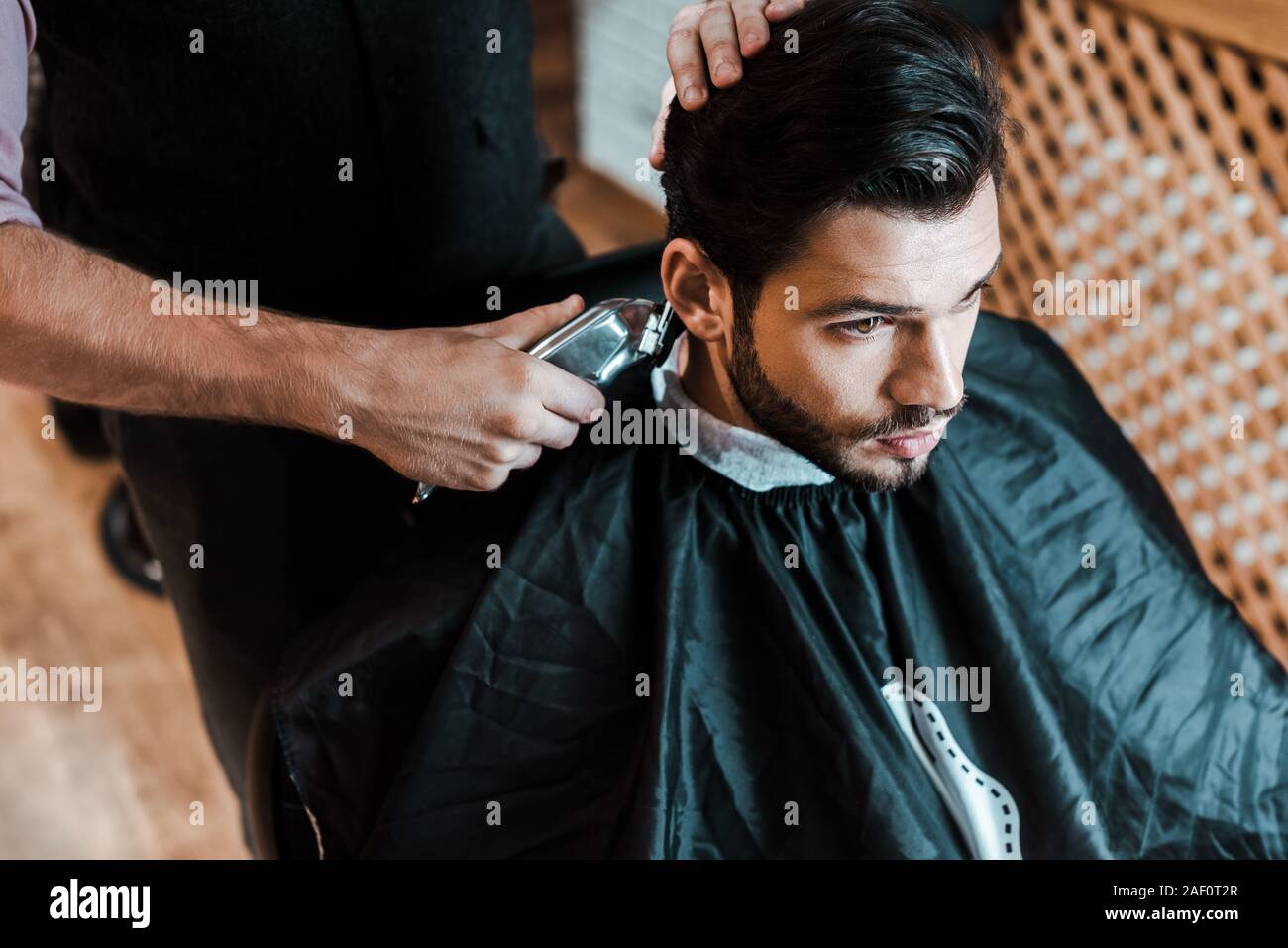 barber holding trimmer while styling hair of handsome man in barbershop Stock Photo