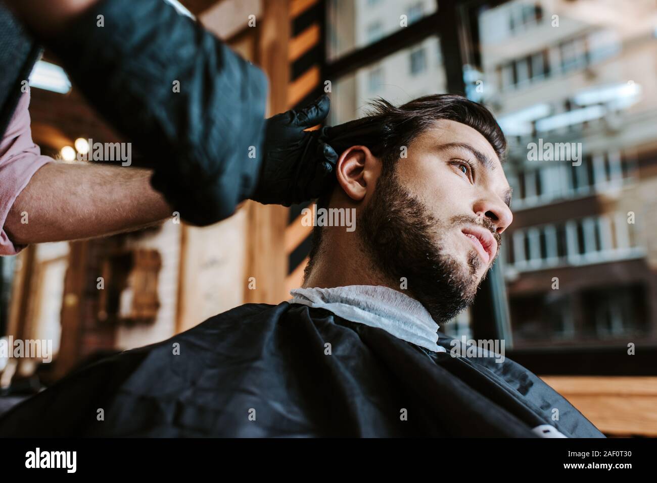 selective focus of barber in latex gloves holding hair comb while styling hair of man Stock Photo