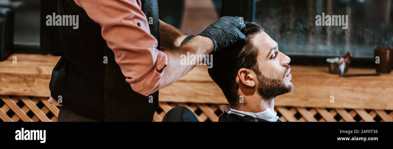 panoramic shot of barber in black latex gloves styling hair of man Stock Photo