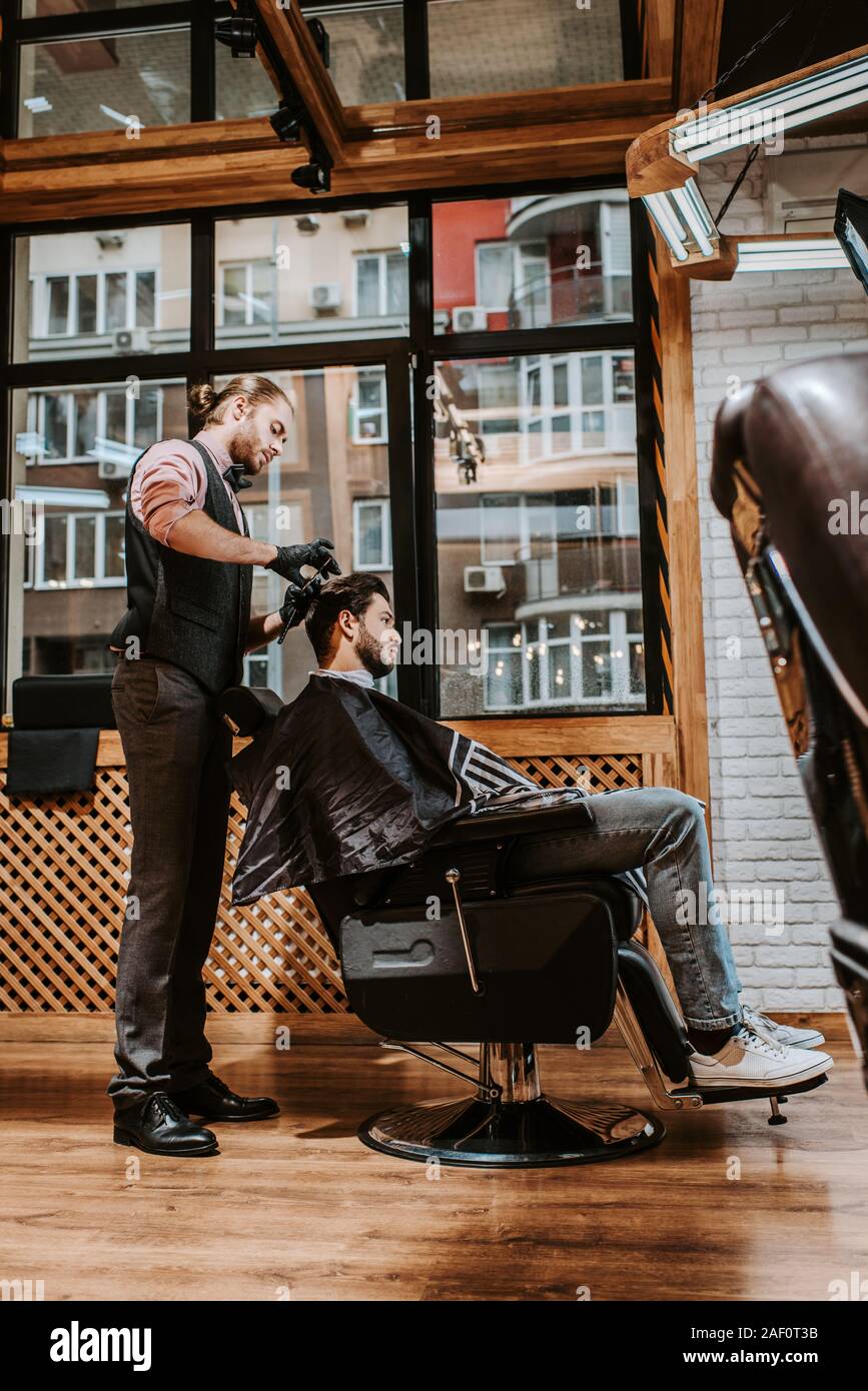 side view of handsome barber styling hair of man in modern barbershop Stock Photo