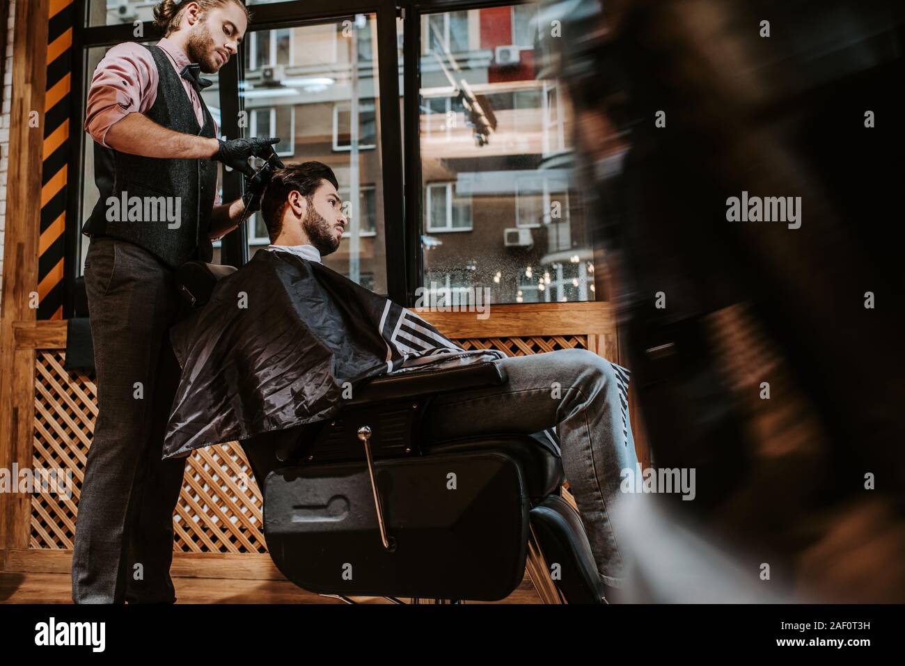side view of handsome barber styling hair of bearded man in modern barbershop Stock Photo