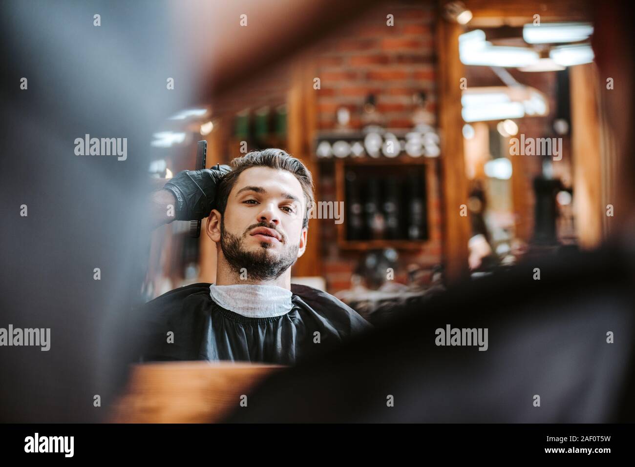 selective focus of barber styling hair of bearded man near mirror in barbershop Stock Photo
