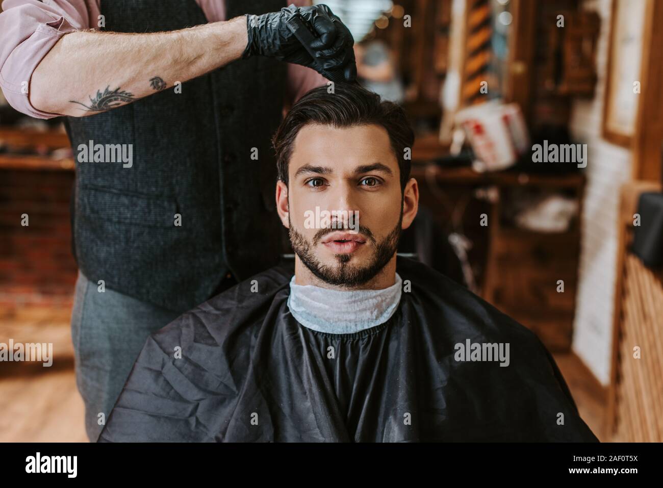 tattooed barber styling hair of bearded man in barbershop Stock Photo