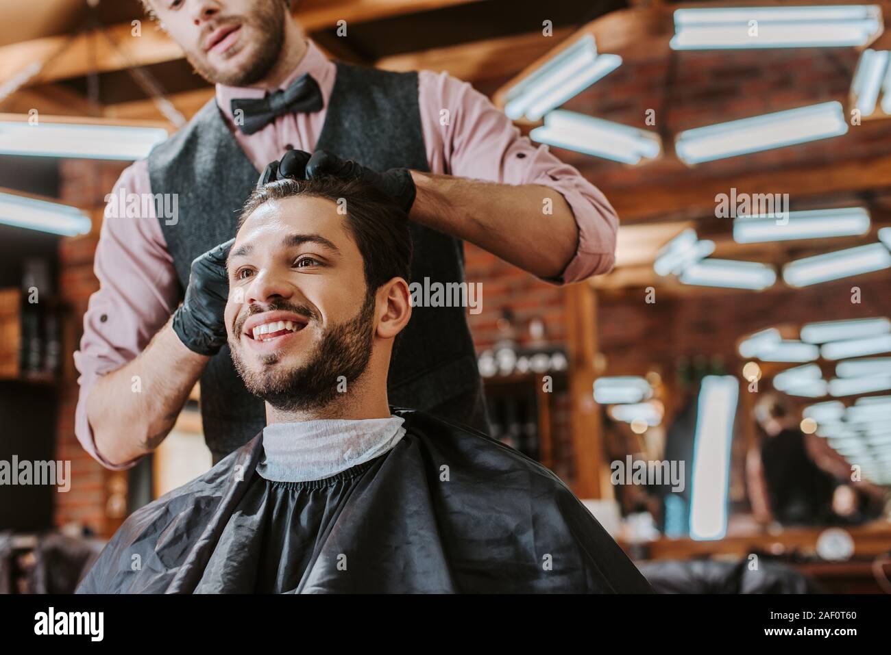 barber in black latex gloves touching hair of happy man in barbershop Stock Photo