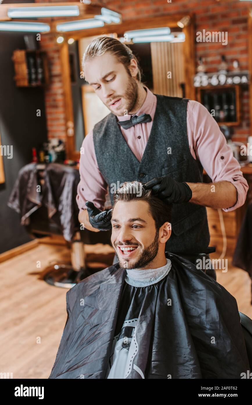 handsome barber in black latex gloves touching hair of happy man in barbershop Stock Photo