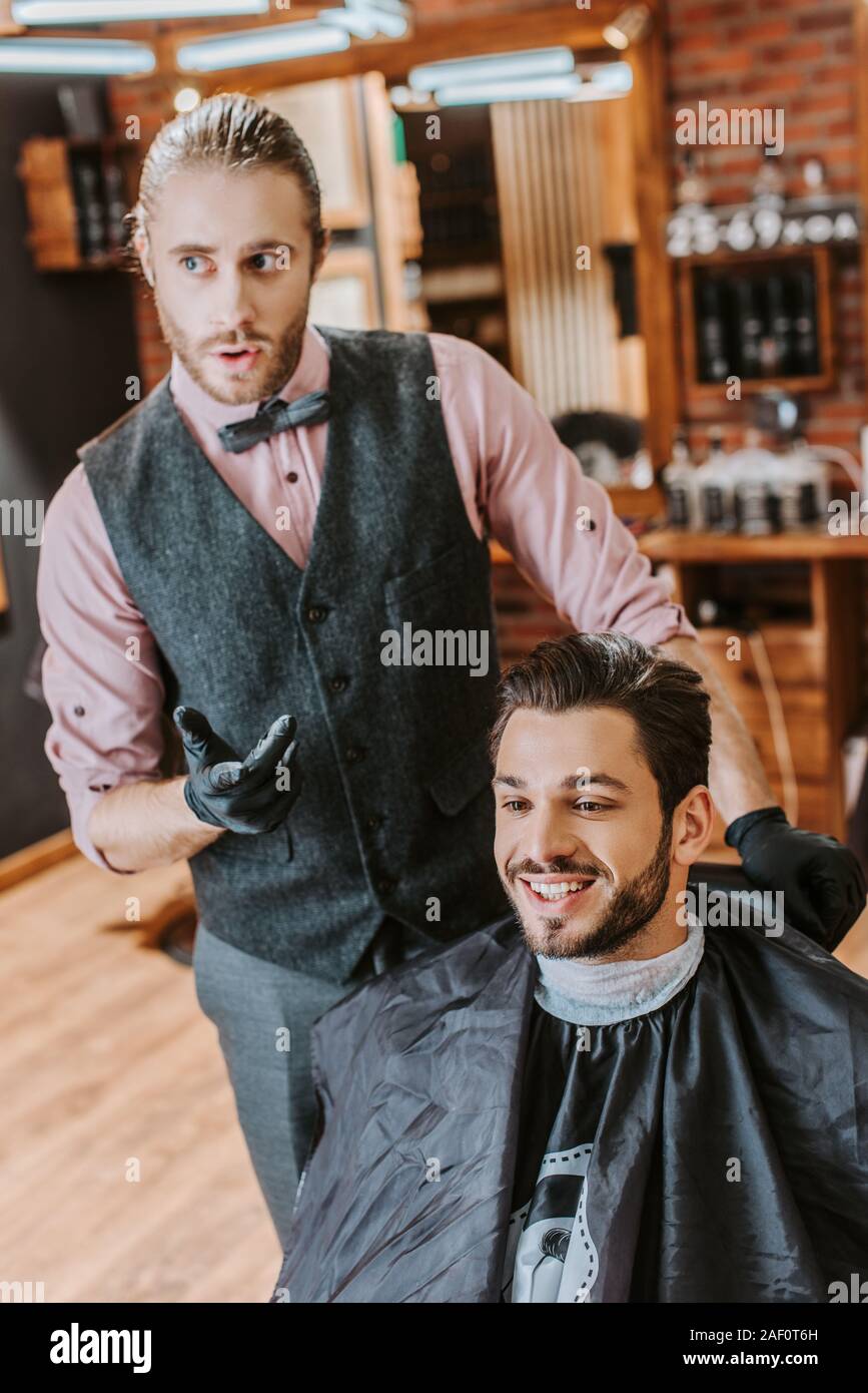 handsome barber gesturing near happy man in barbershop Stock Photo