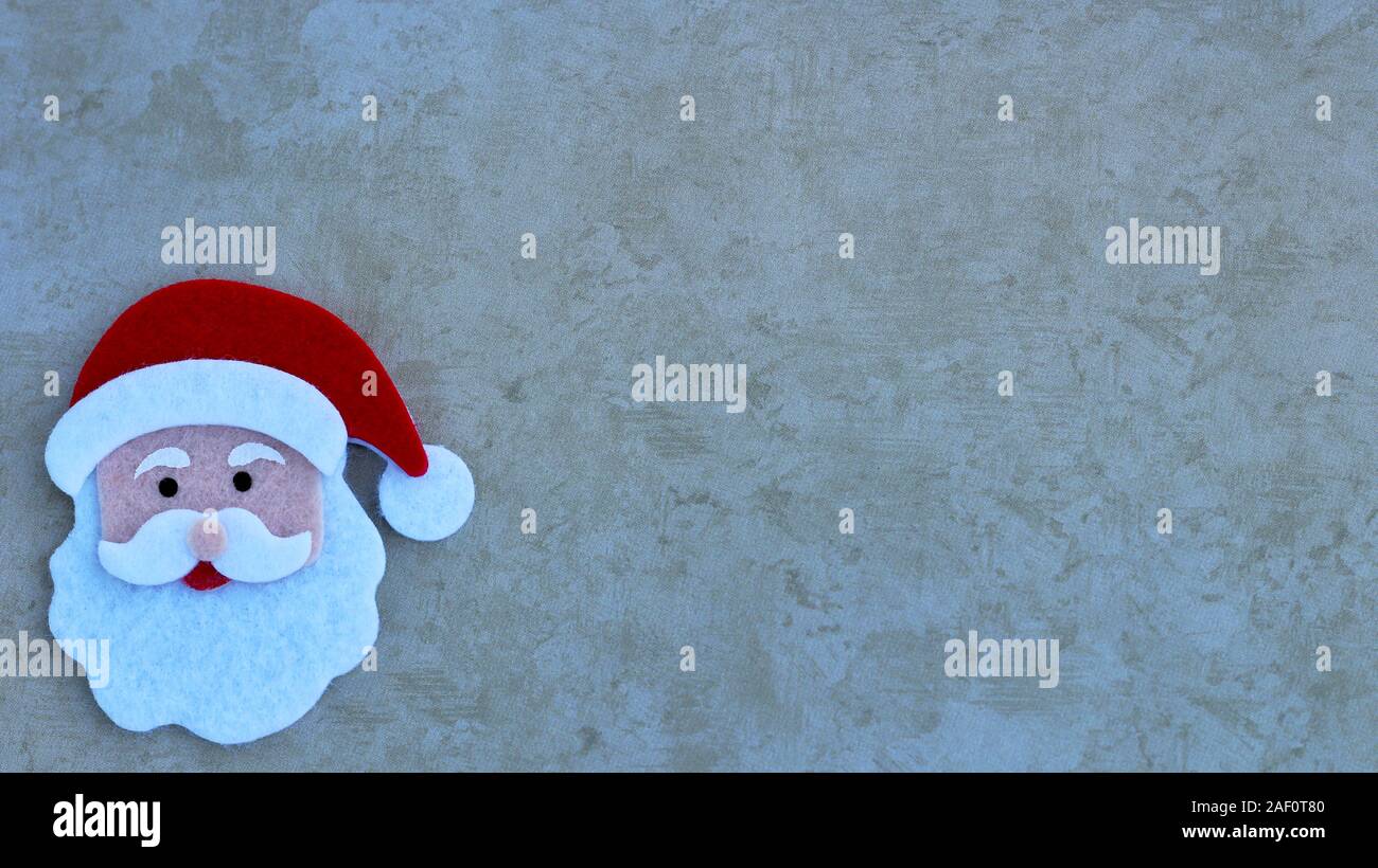 felt crafted Santa Claus face with hat, beard and mustache on a tan background with copy space Stock Photo