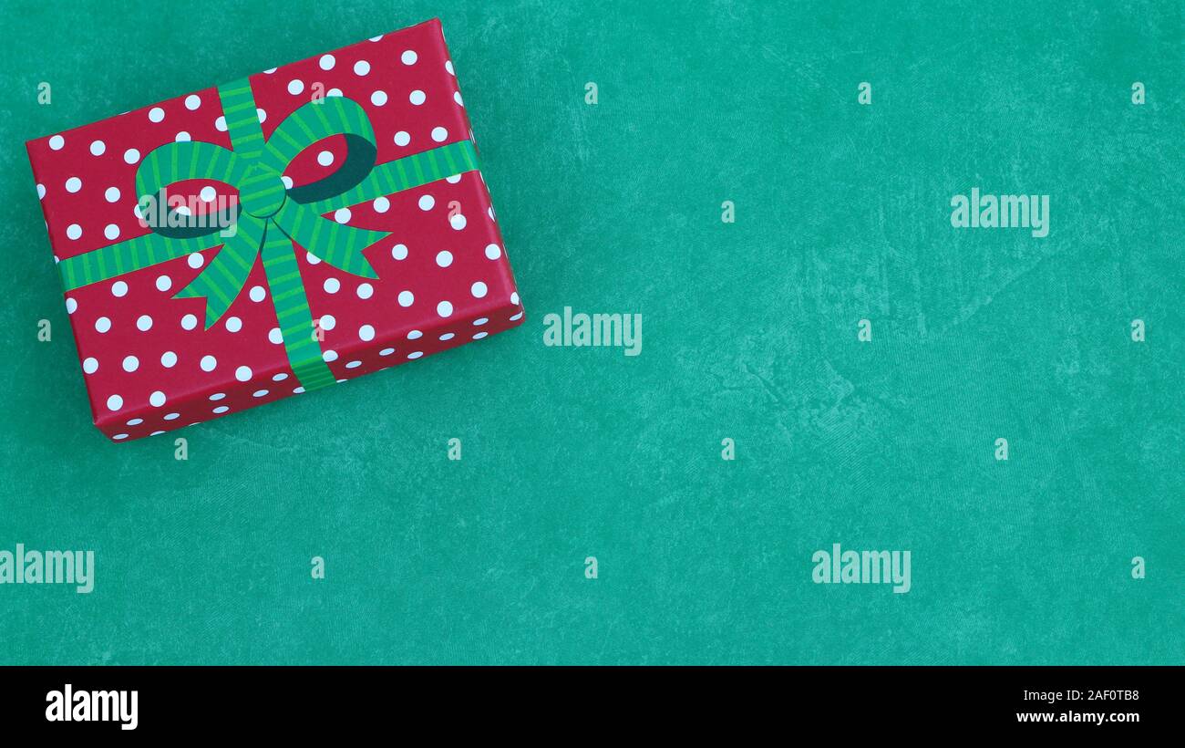 top view of wrapped red and white polka dot gift box with a green bow on a festive green background with copy space Stock Photo