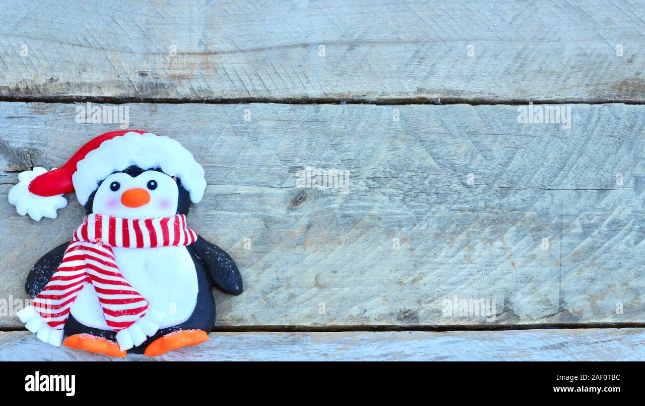 penguin with Santa Claus hat, striped red and white scarf, and orange feet laying flat on natural wood background with copy space Stock Photo