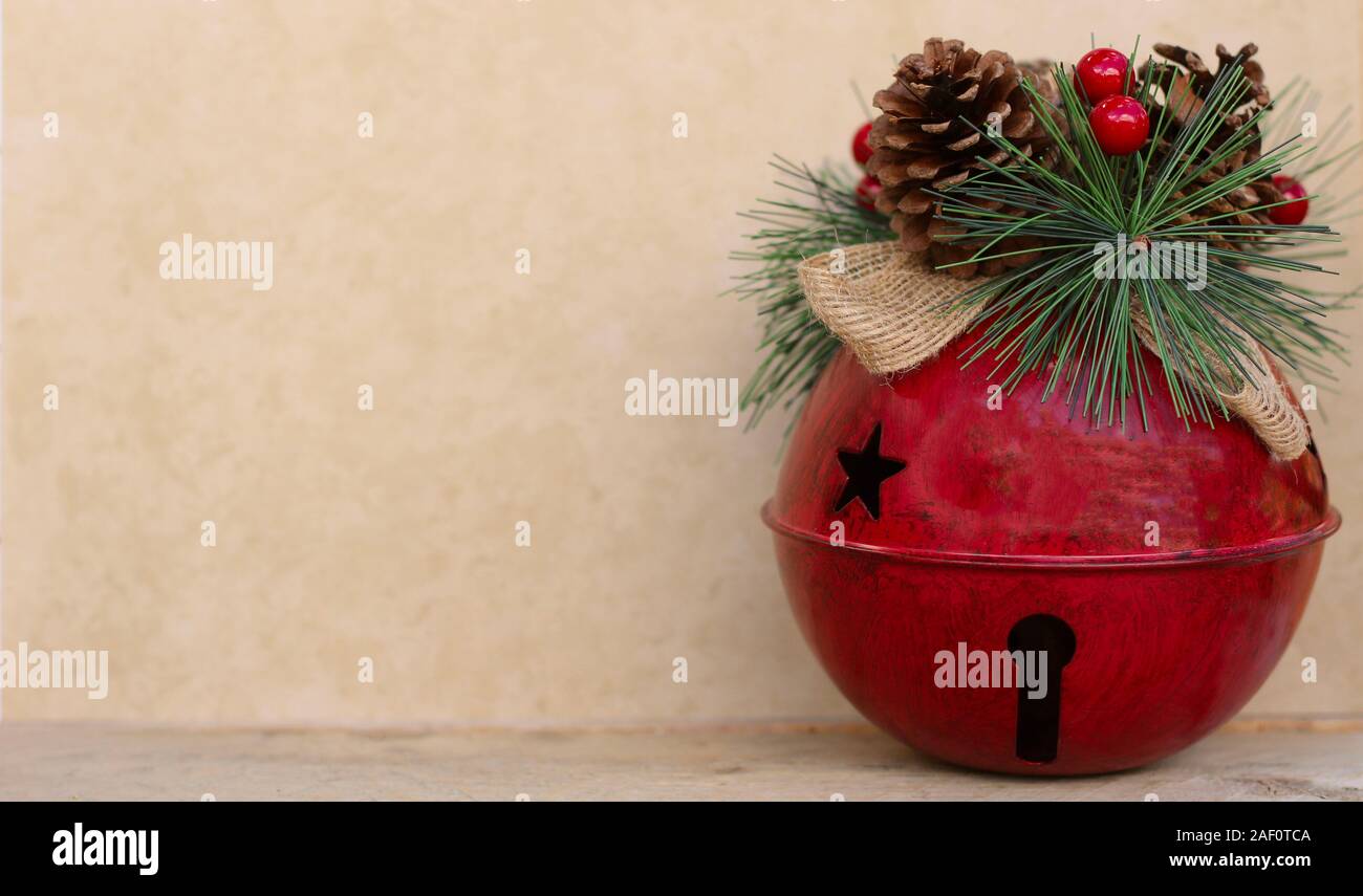 large red jingle bell decorated with pine cone, berries and raffia bow on a tan background with copy space Stock Photo