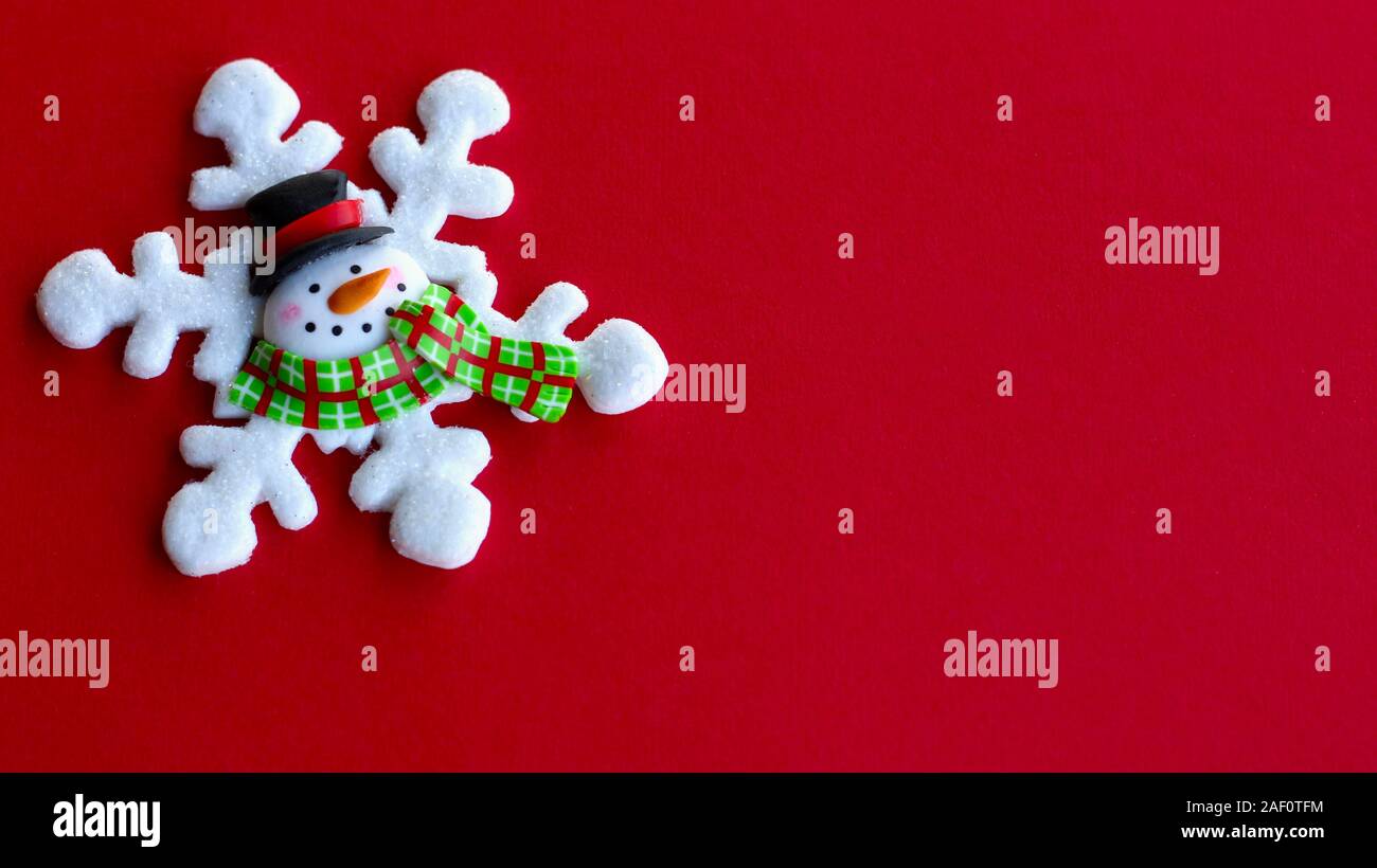 white snowflake decorated with a snowman face in the center wearing a hat and scarf on a red background with copy space Stock Photo