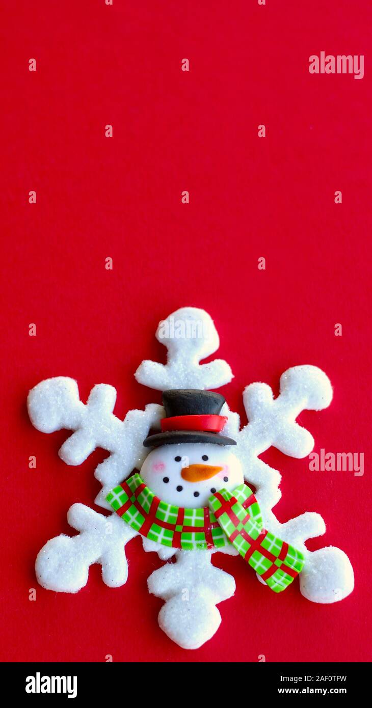 white snowflake decorated with a snowman face in the center wearing a hat and scarf on a vertical red background with copy space Stock Photo