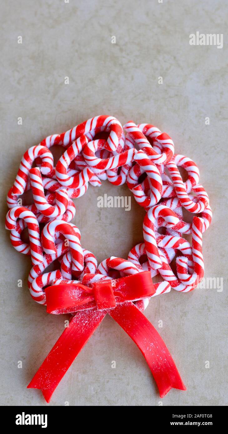 red and white candy cane wreath with a red bow laying flat on a tan color background with writing space, vertical Stock Photo