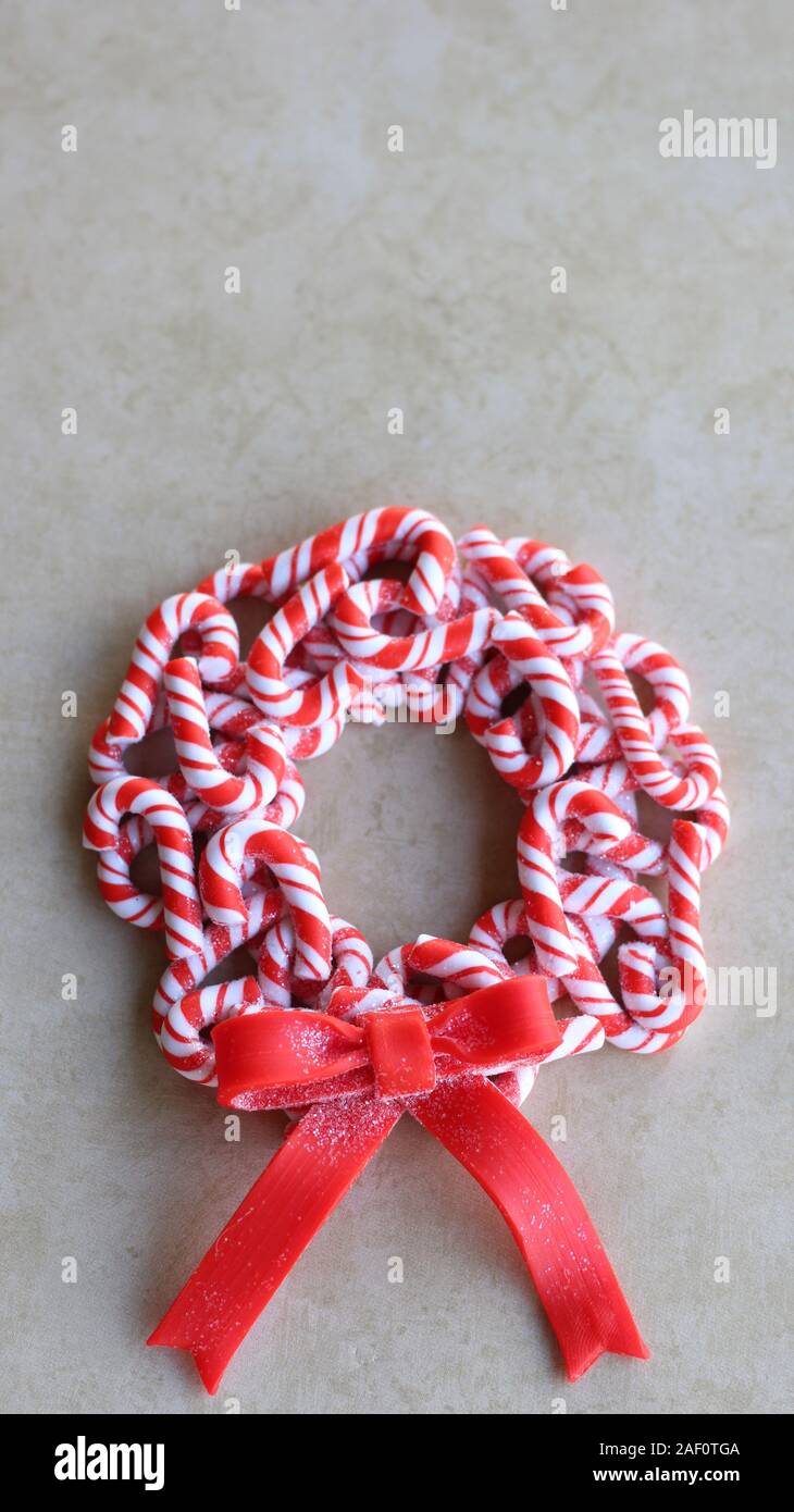 red and white candy cane wreath with a red bow laying flat on a tan color background with writing spa Stock Photo