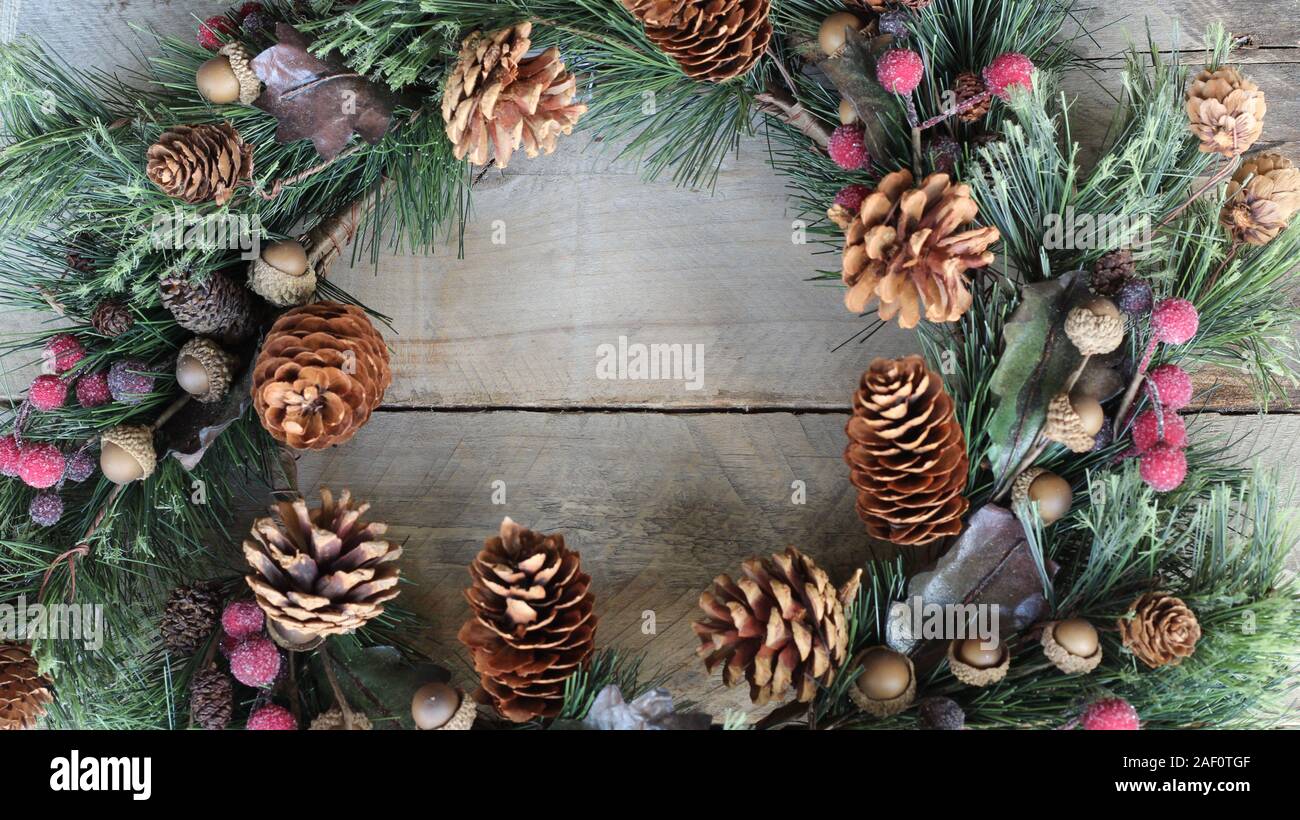 Pine wreath with pine cones berries and acorns laying flat on a wood background with copy space Stock Photo