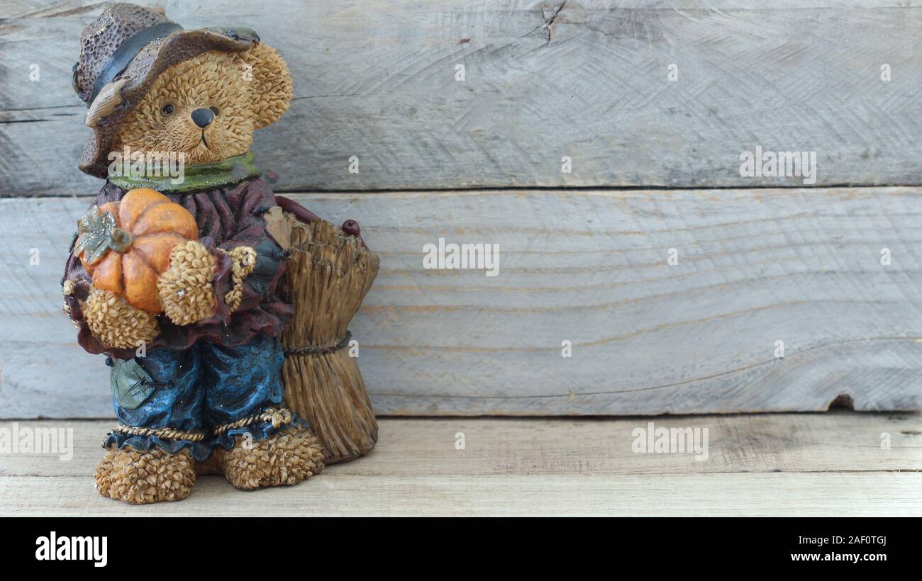 autumn teddy bear dressed in blue overalls wearing a farmer hat holding a pumpkin standing on a wood background with copy space Stock Photo