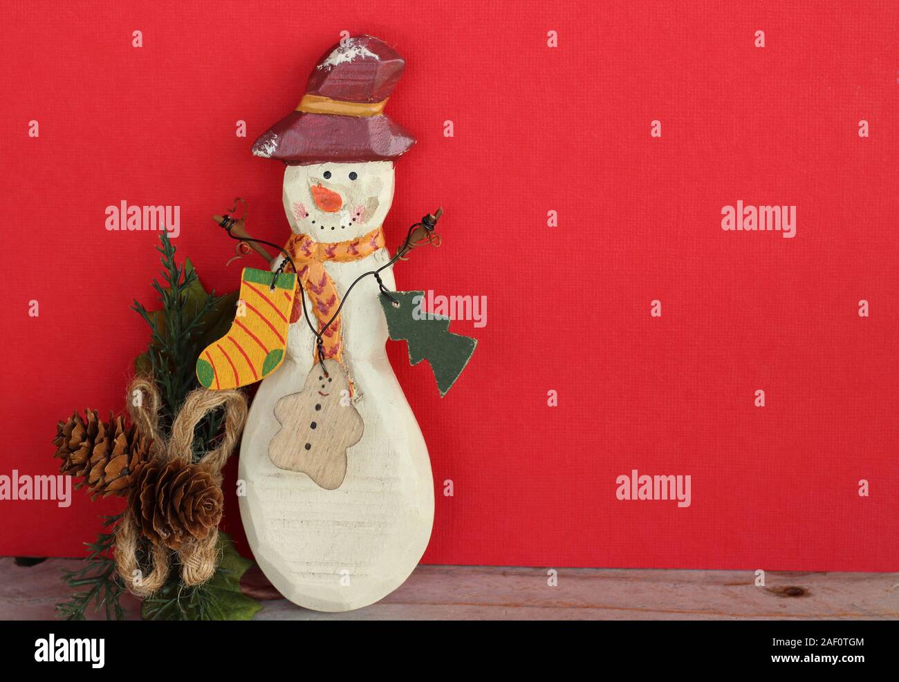 wooden decorated primitive snowman with a red hat and decorated scarf standing on a red background with copy space Stock Photo