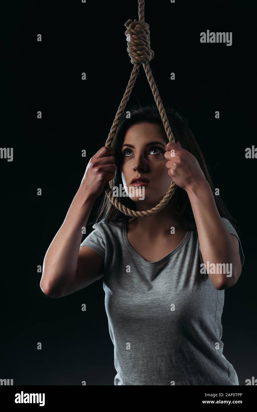 frustrated young woman committing suicide while putting hanging rope noose on head isolated on black Stock Photo