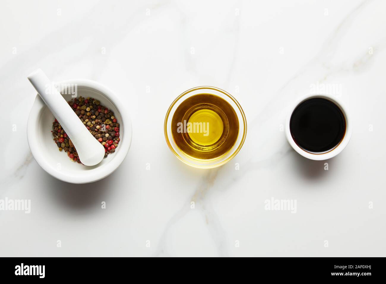 Top view of olive oil, soy sauce and peppercorns in bowls on marble