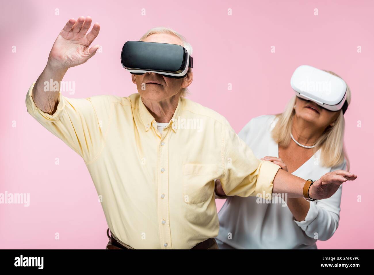 retired man gesturing while wearing virtual reality headset near wife on pink Stock Photo