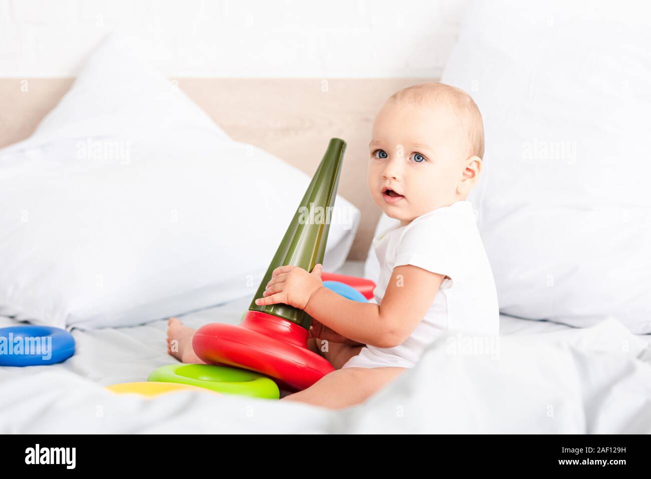 https://c8.alamy.com/comp/2AF129H/adorable-little-child-in-white-clothes-sitting-on-bed-and-holding-colorful-toy-pyramid-2AF129H.jpg