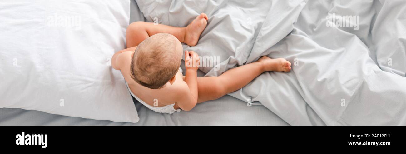 Panoramic shot of little barefoot child sitting on bed with white bedding Stock Photo