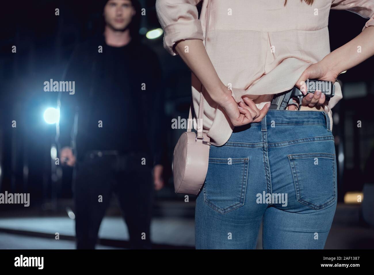 back view of woman hiding gun behind back near thief at night Stock