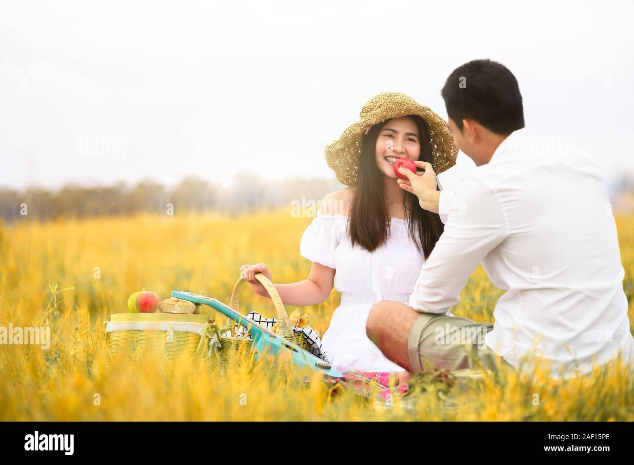 Asian couple doing picnic in golden autumn meadow grass field as honeymoon trip after wedding. Valentines day and family love concept. Outdoors nature Stock Photo