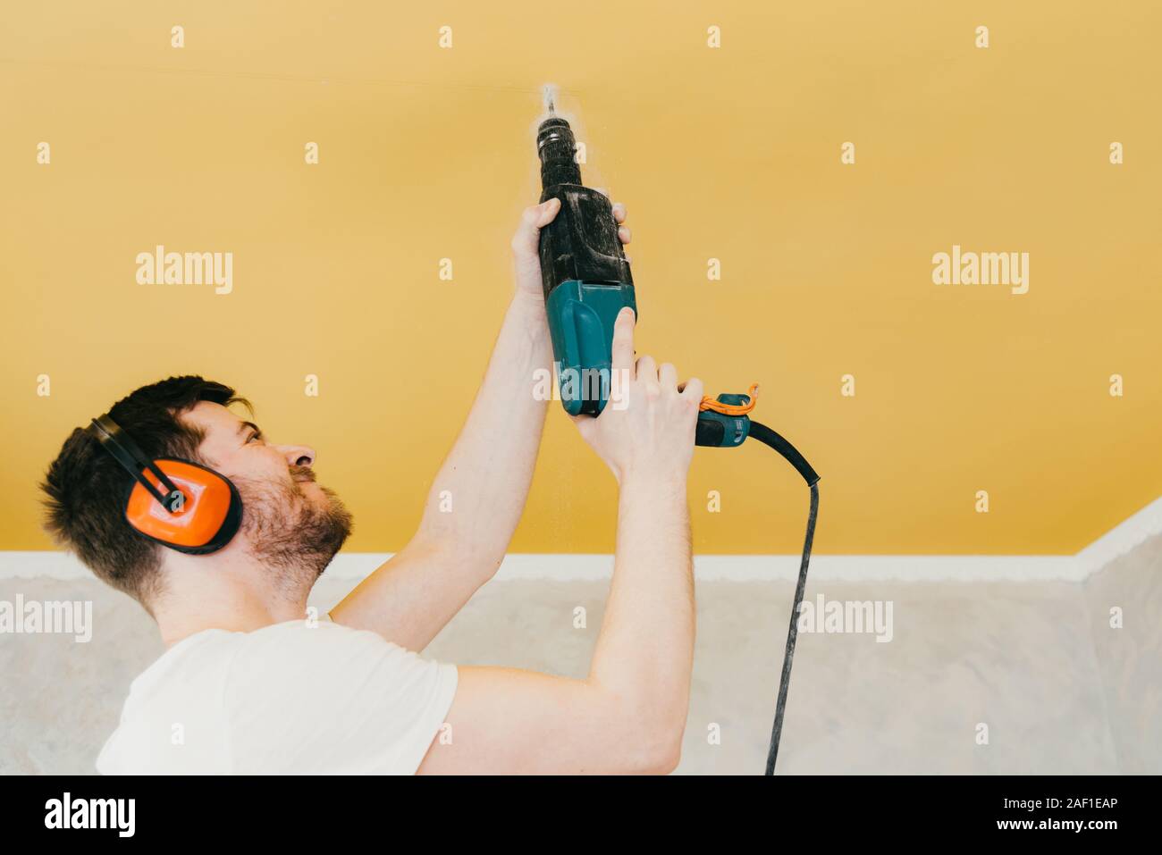 the guy is drilling a hole in the ceiling with a drill in his apartment Stock Photo