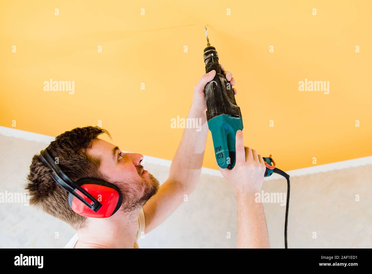 the guy is drilling a hole in the ceiling with a drill in his apartment Stock Photo