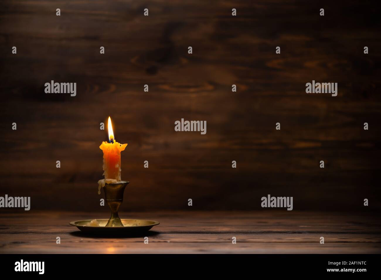 burning old candle with vintage brass candlestick on wooden background