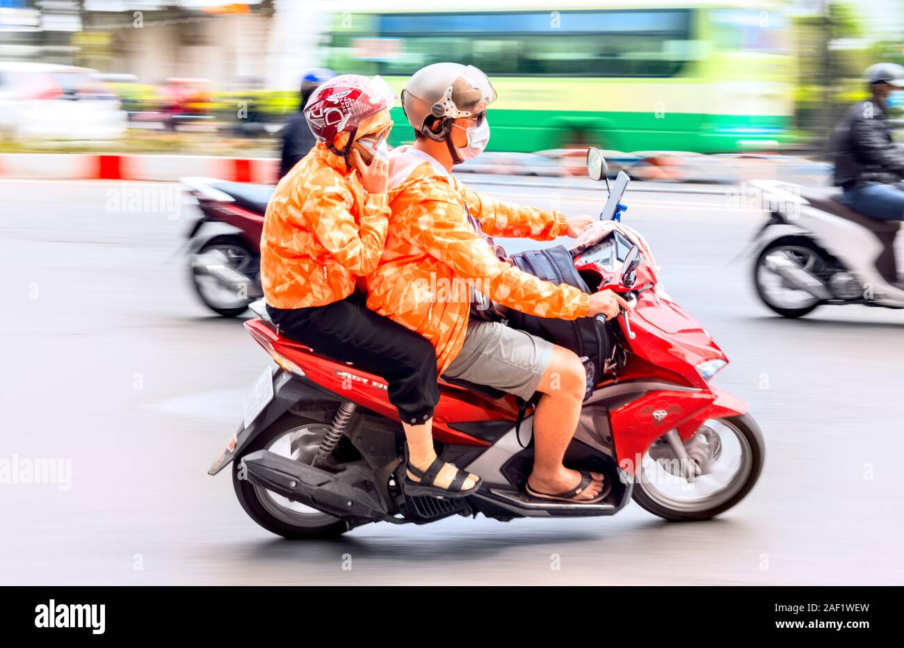 Ho Chi Minh City formerly Saigon 2 people wearing matching clothes riding moped Stock Photo